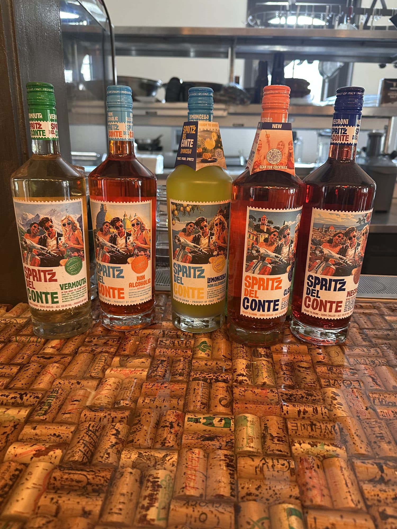 A row of spritz aperitivo bottles on a wine-cork bar top